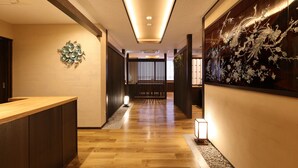 A hallway with wooden flooring, a reception desk, a decorative wall with a floral pattern, and a traditional sliding door in the background. - Mutsumikan (Gero)