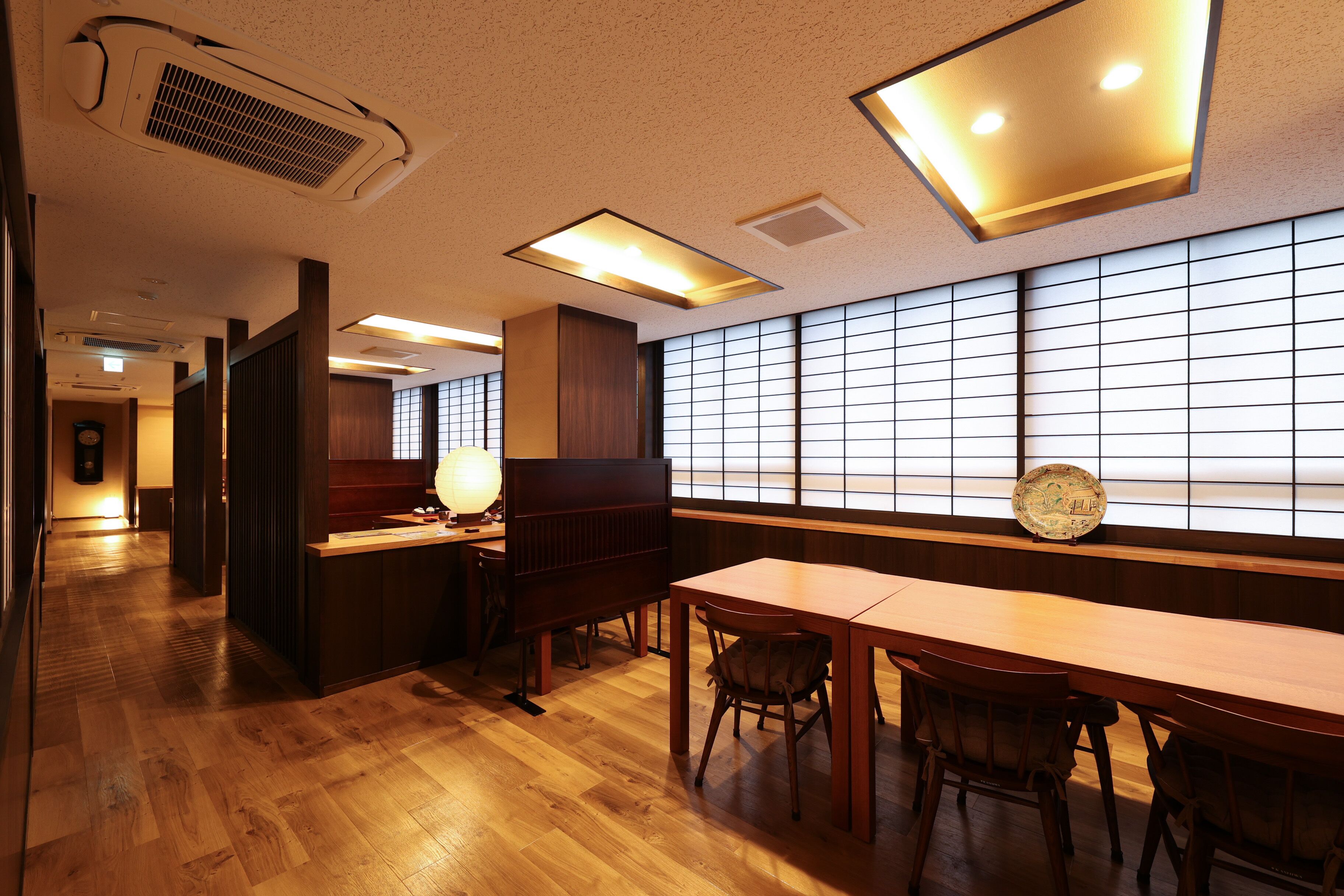 A traditional Japanese-style room with wooden flooring, tatami mats, low tables, and sliding doors.