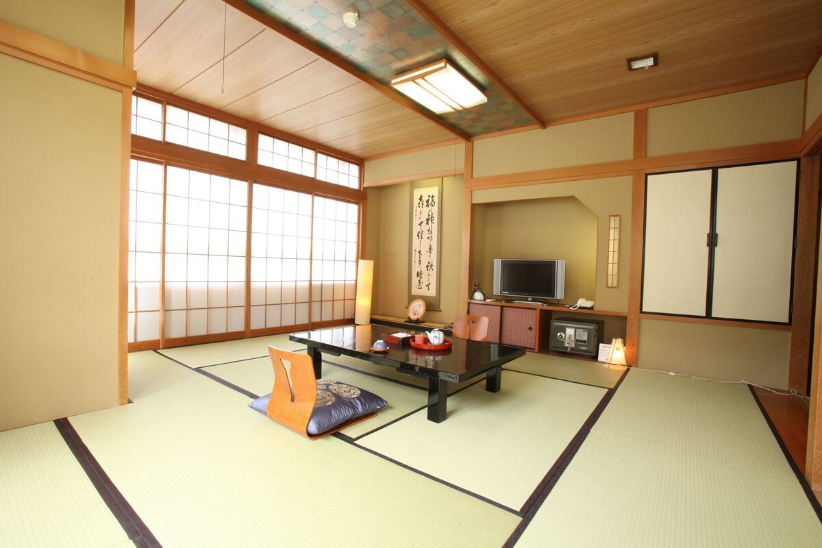 A traditional Japanese room with tatami flooring, a low table, a television, and sliding doors.