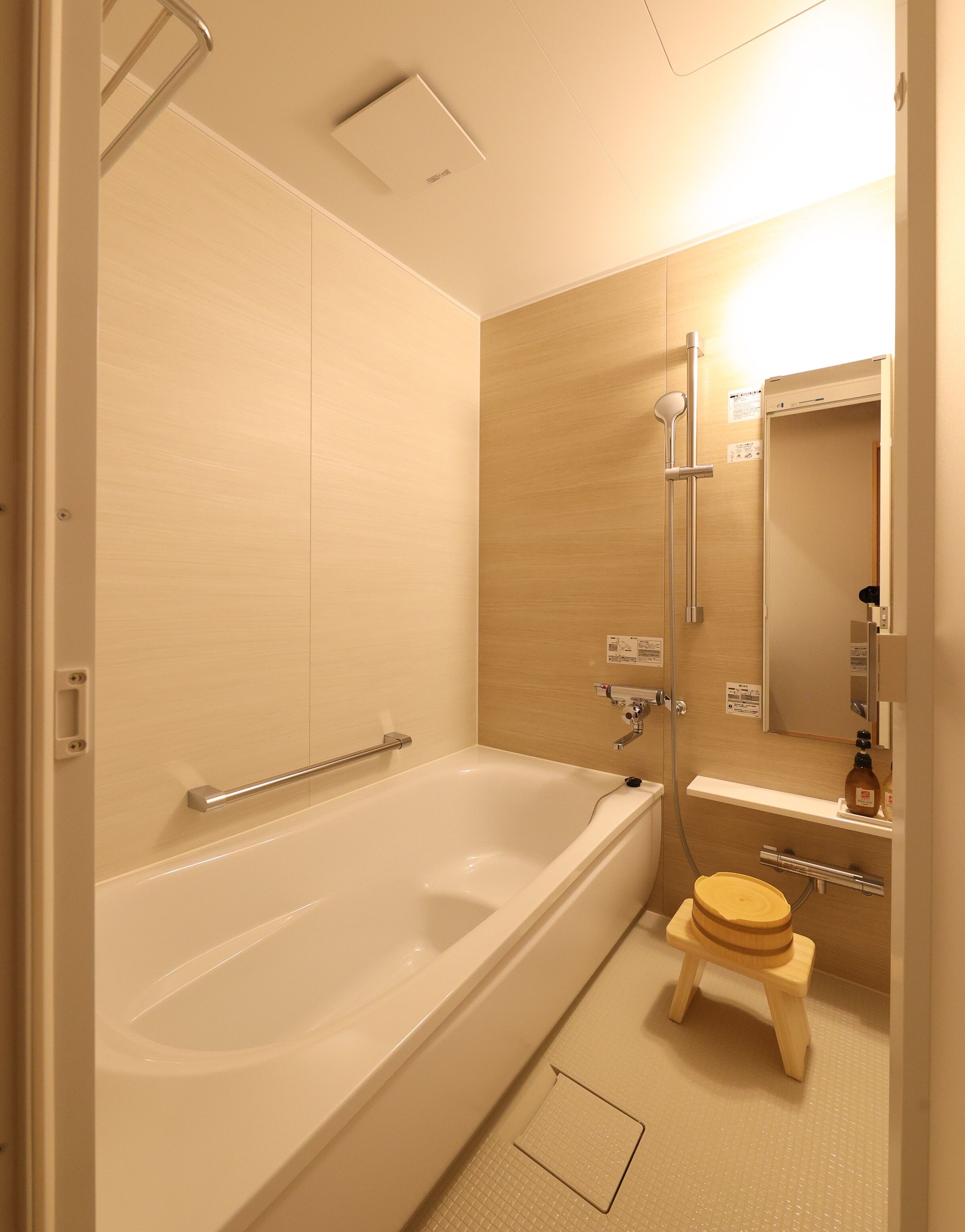 Un baño moderno con bañera, ducha, inodoro y un pequeño taburete de madera.