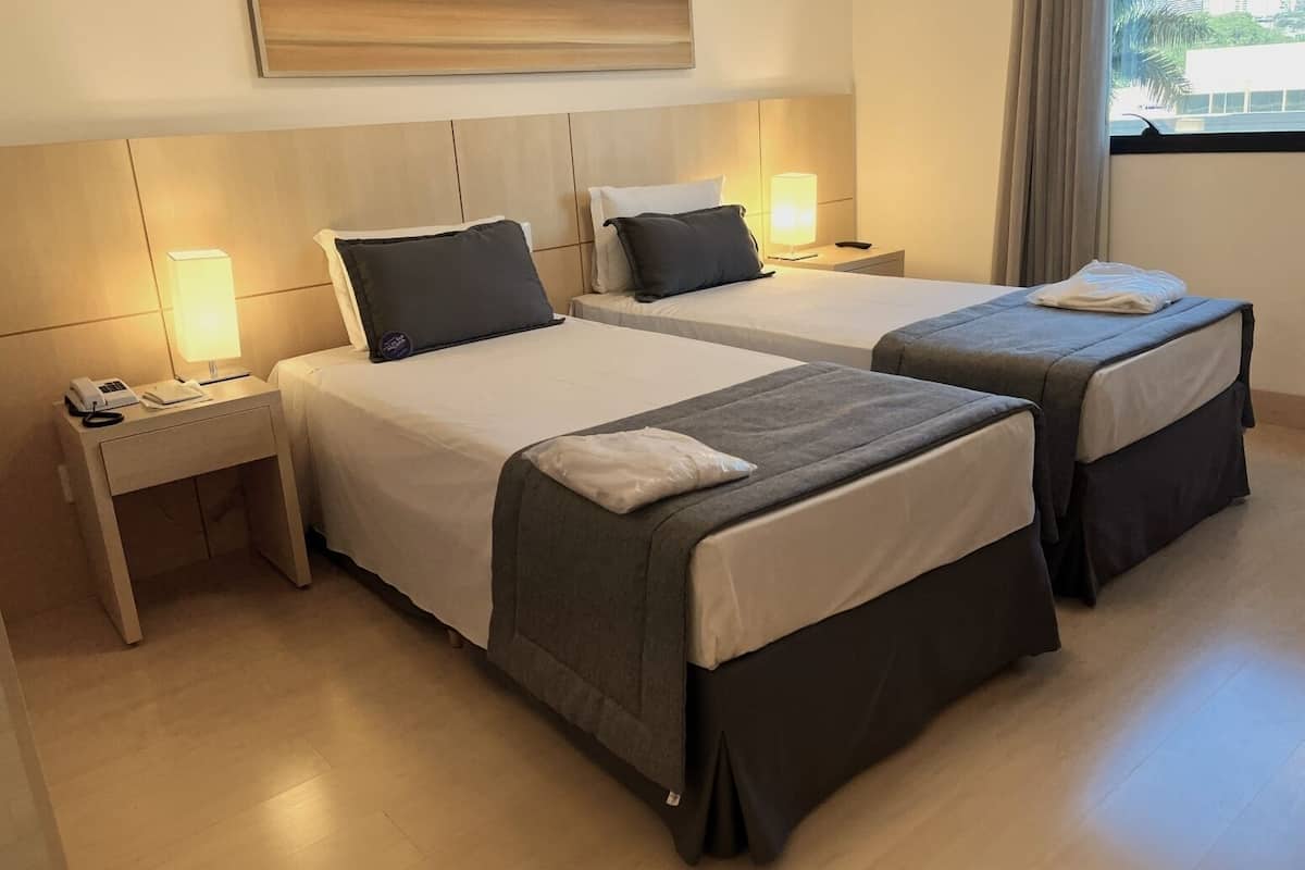 A hotel room with two beds, a bedside table with a phone, and a lamp.
