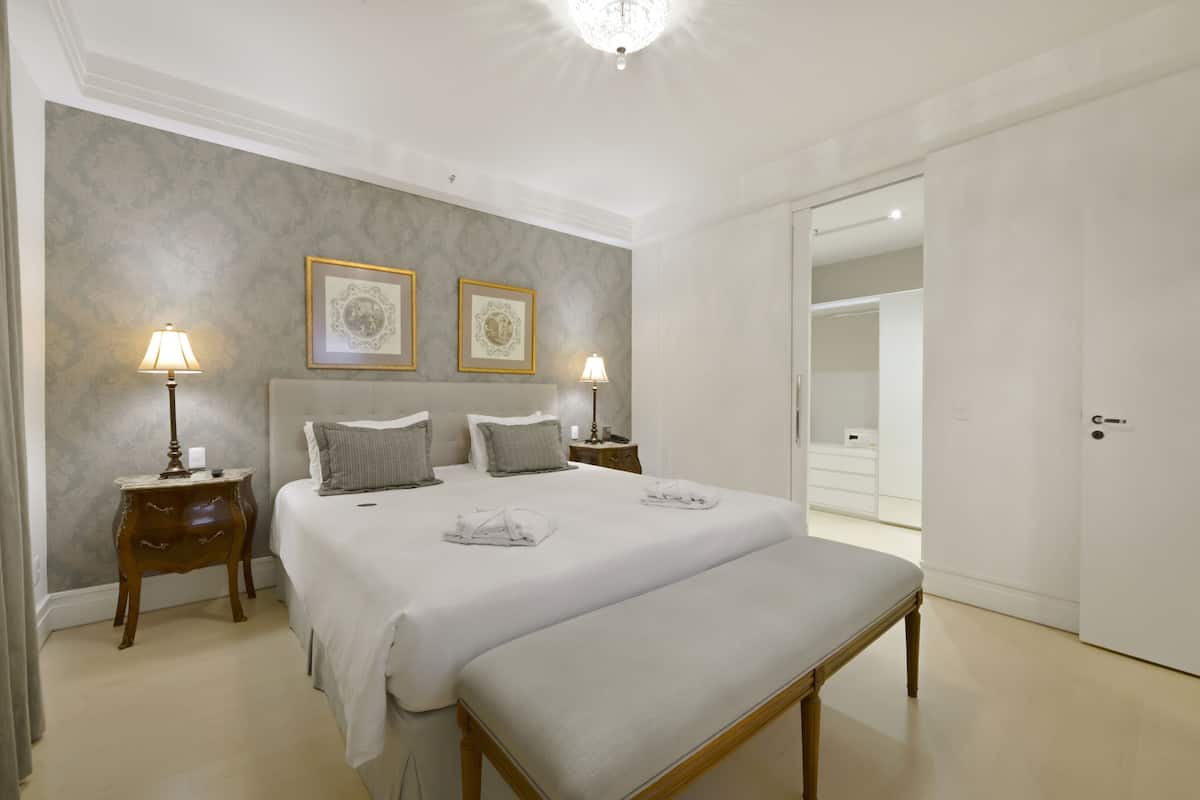 A neatly arranged bedroom with a large bed, two bedside tables with lamps, and a bench.
