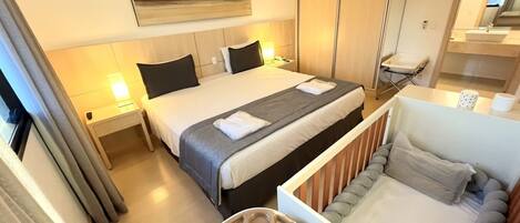 A hotel room with a bed, bedside tables, a desk, a chair, and a small table with a tray.