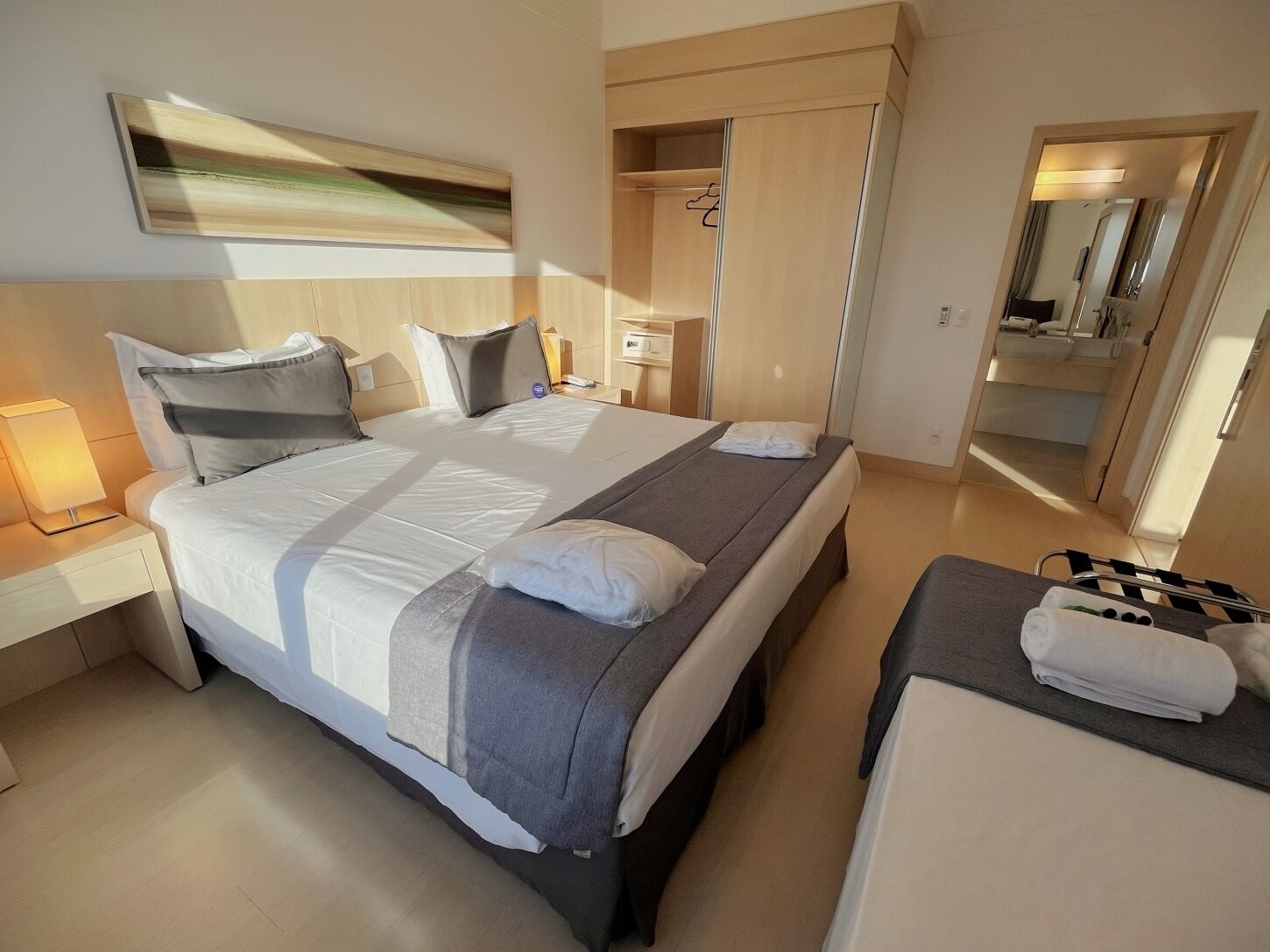 A modern hotel room with a large bed, bedside tables, a small desk, and a bathroom visible through an open door.