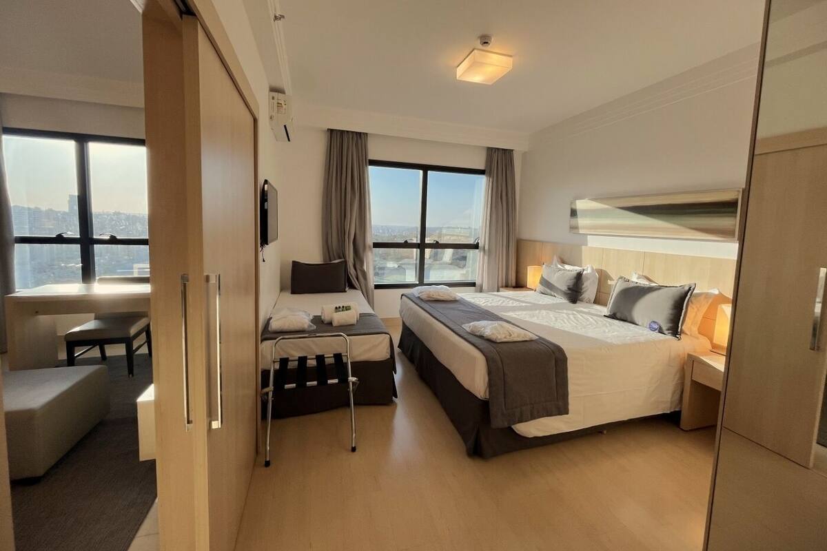 A modern hotel room with a large bed, a desk, and a view of the city.