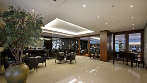 Un moderno vestíbulo de hotel con una planta grande en maceta, zona de estar y un bar.