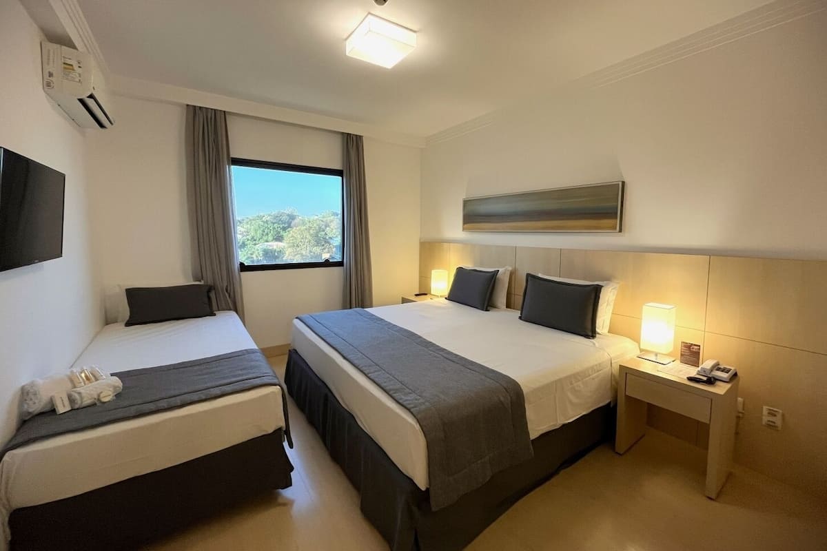 A hotel room with two beds, a TV, a window with a view, a painting on the wall, and a desk with a lamp and phone.