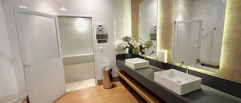 A modern bathroom with a large mirror, two sinks, a shower, and a toilet.