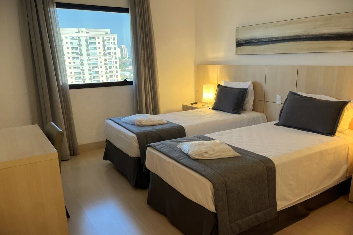 A hotel room with two beds, a desk, and a window with curtains.