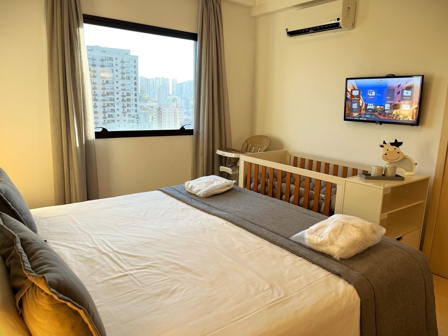 A hotel room with a bed, a crib, a TV, and a window with curtains.