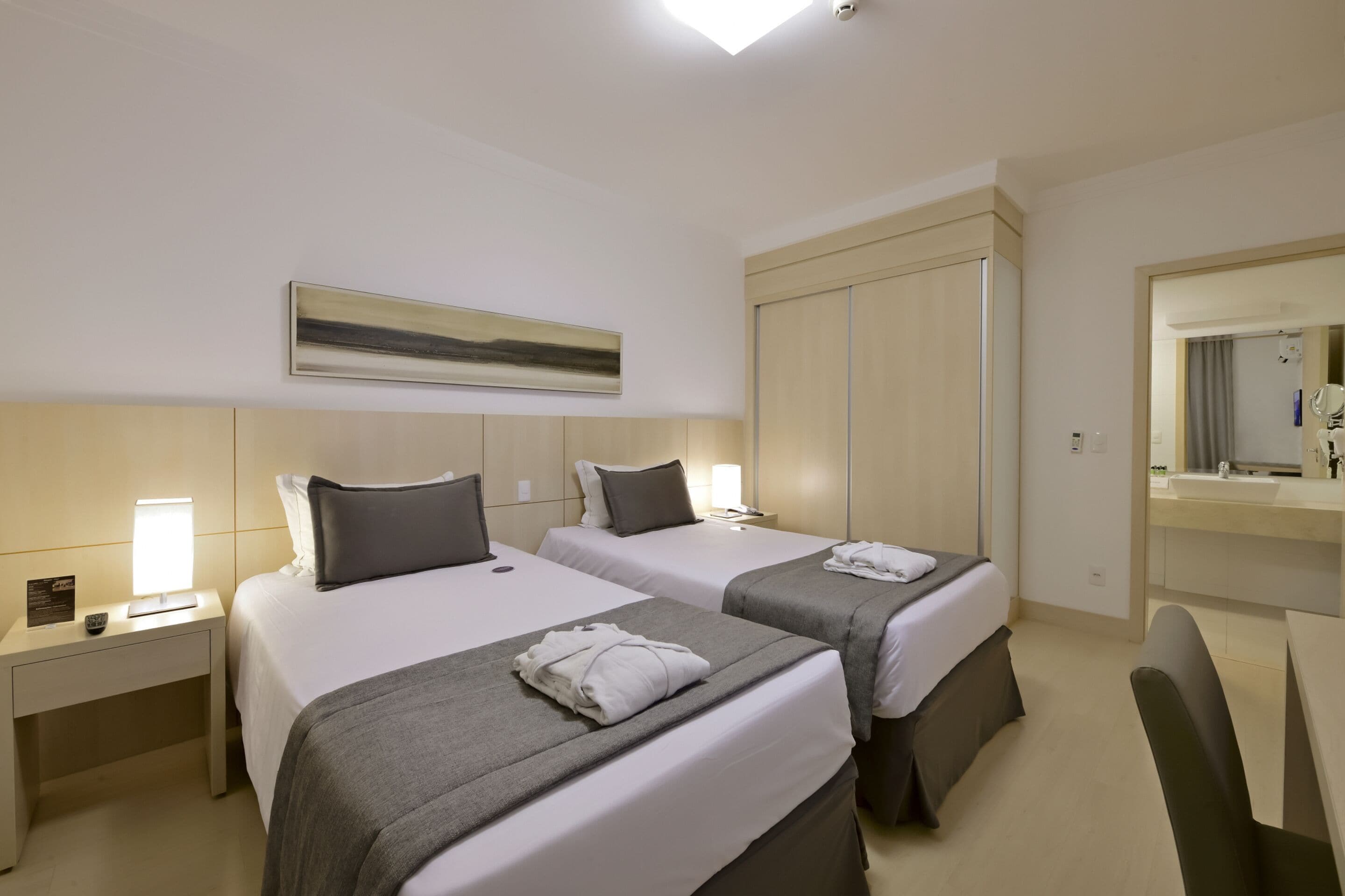 Una habitación de hotel con dos camas, un escritorio, un espejo y un armario.