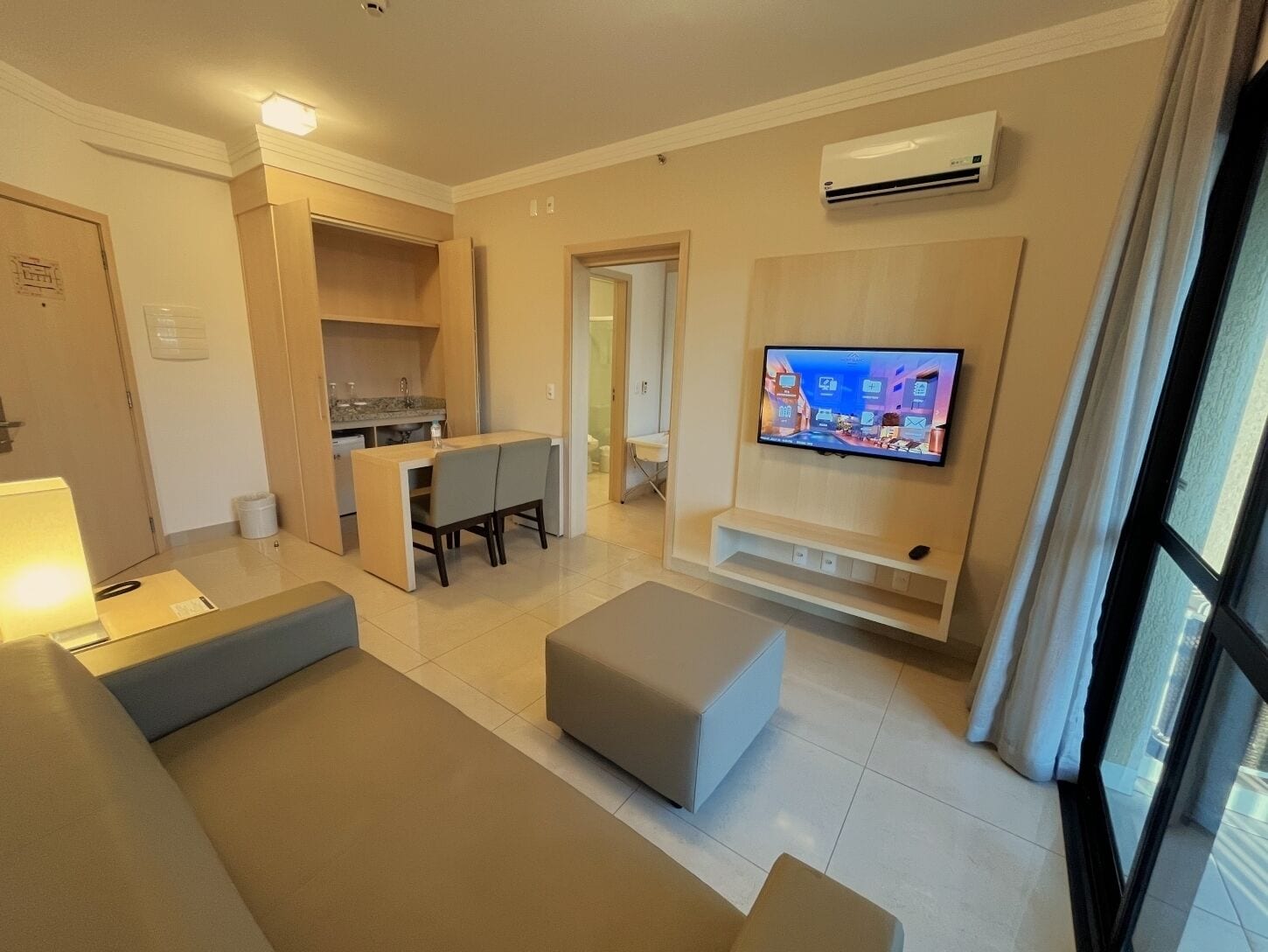 A modern living room with a sofa, ottoman, and a flat-screen TV mounted on the wall.