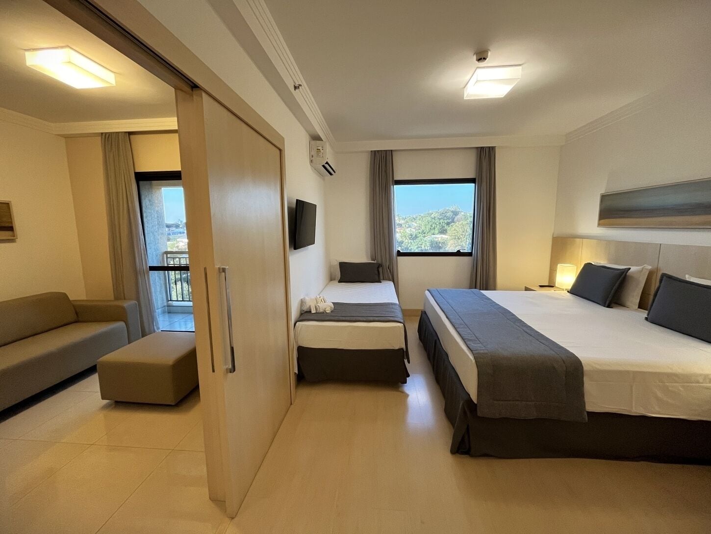 Quarto de hotel com duas camas, um sofá, uma televisão e uma varanda.