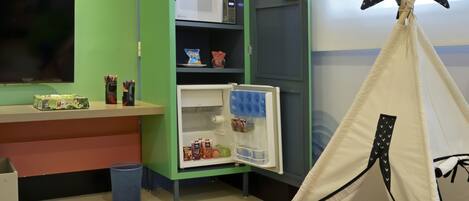 A room with a play area, including a colorful foam mat, a bookshelf, a tent, and a television.
