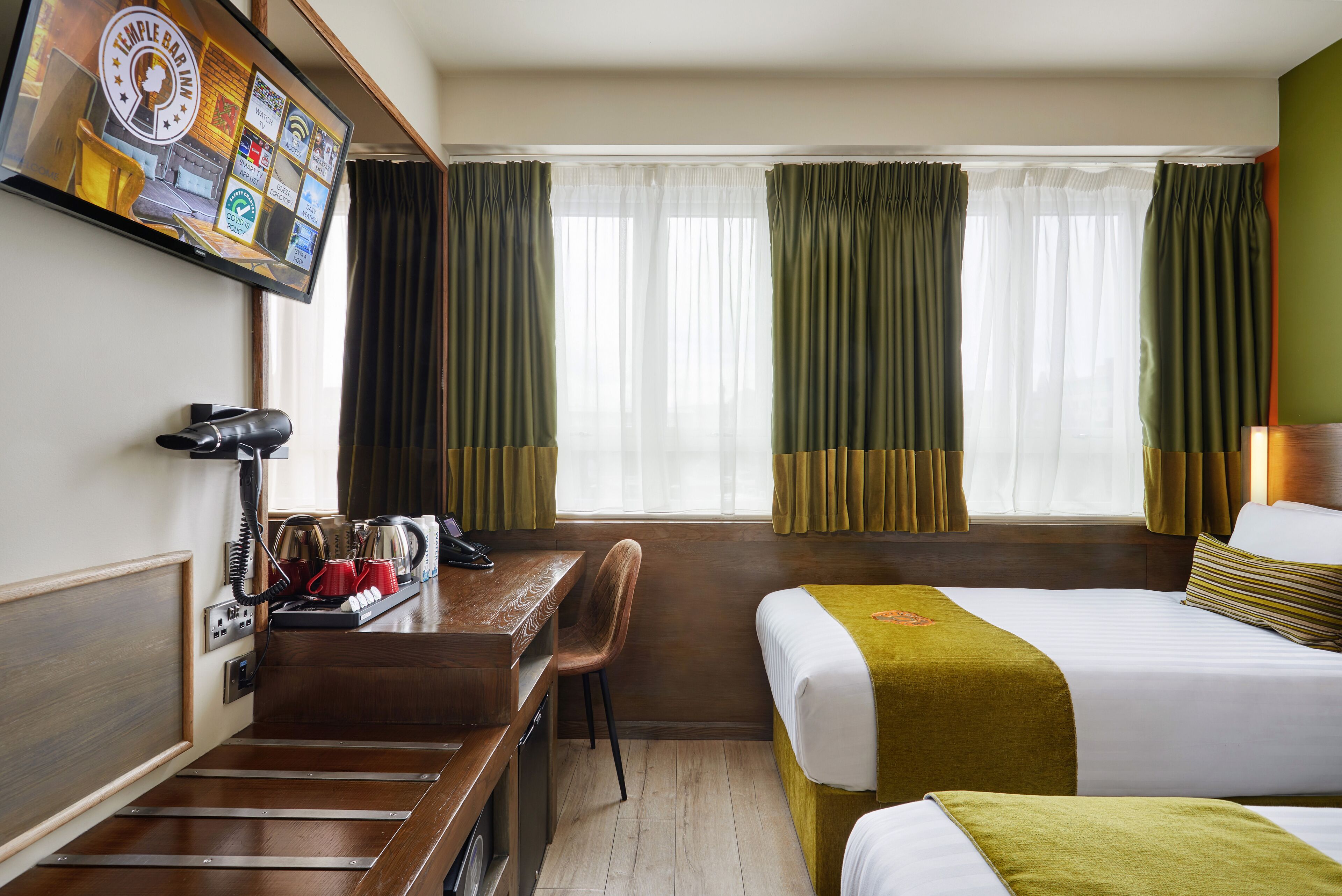 Una habitación de hotel con escritorio, silla, dos camas, televisor y ventana con cortinas.