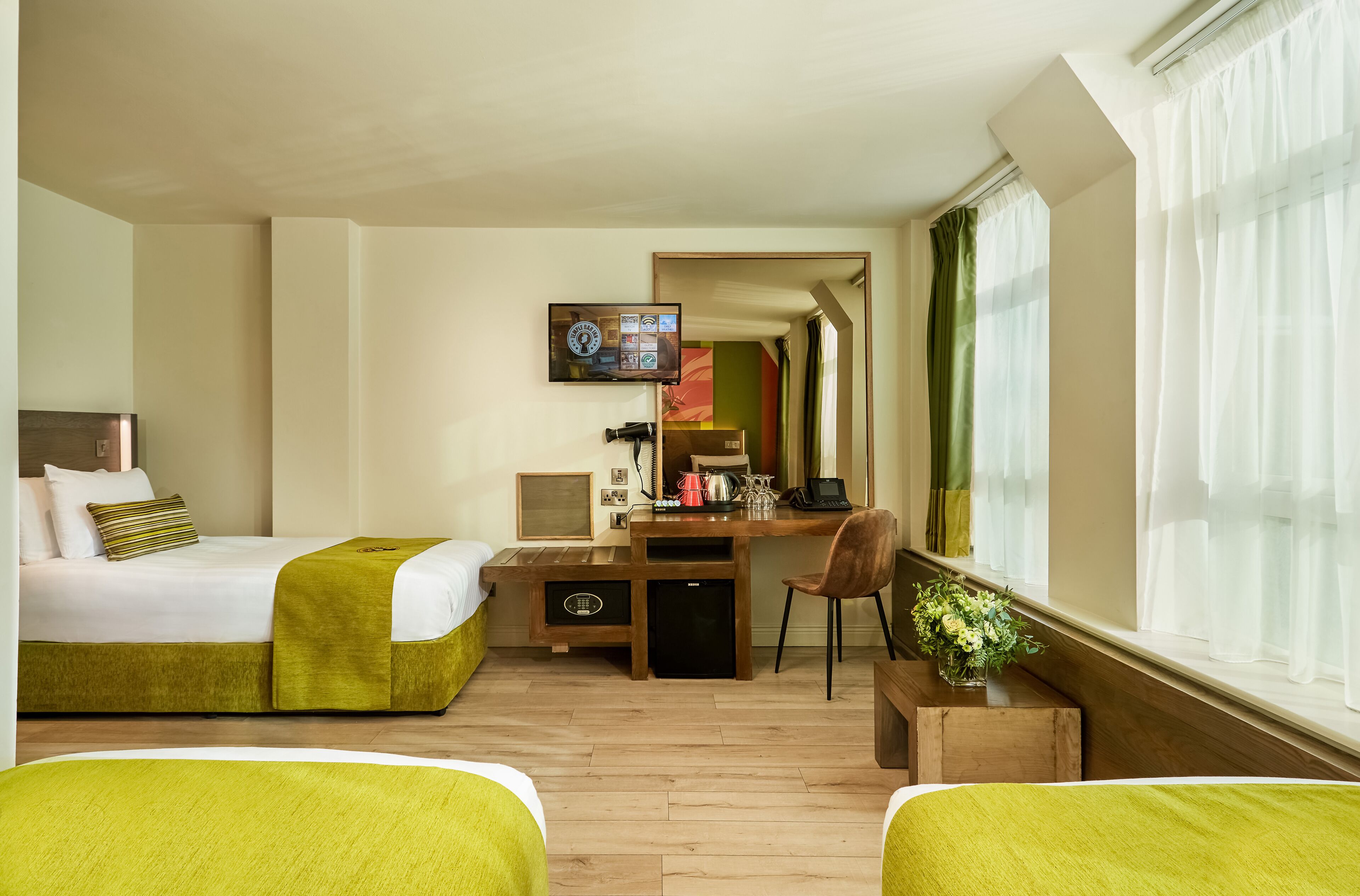 A hotel room with two beds, a desk, a chair, a TV, and a window with curtains.