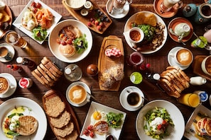 A variety of breakfast dishes, including pancakes, eggs, and pastries, arranged on a wooden table.