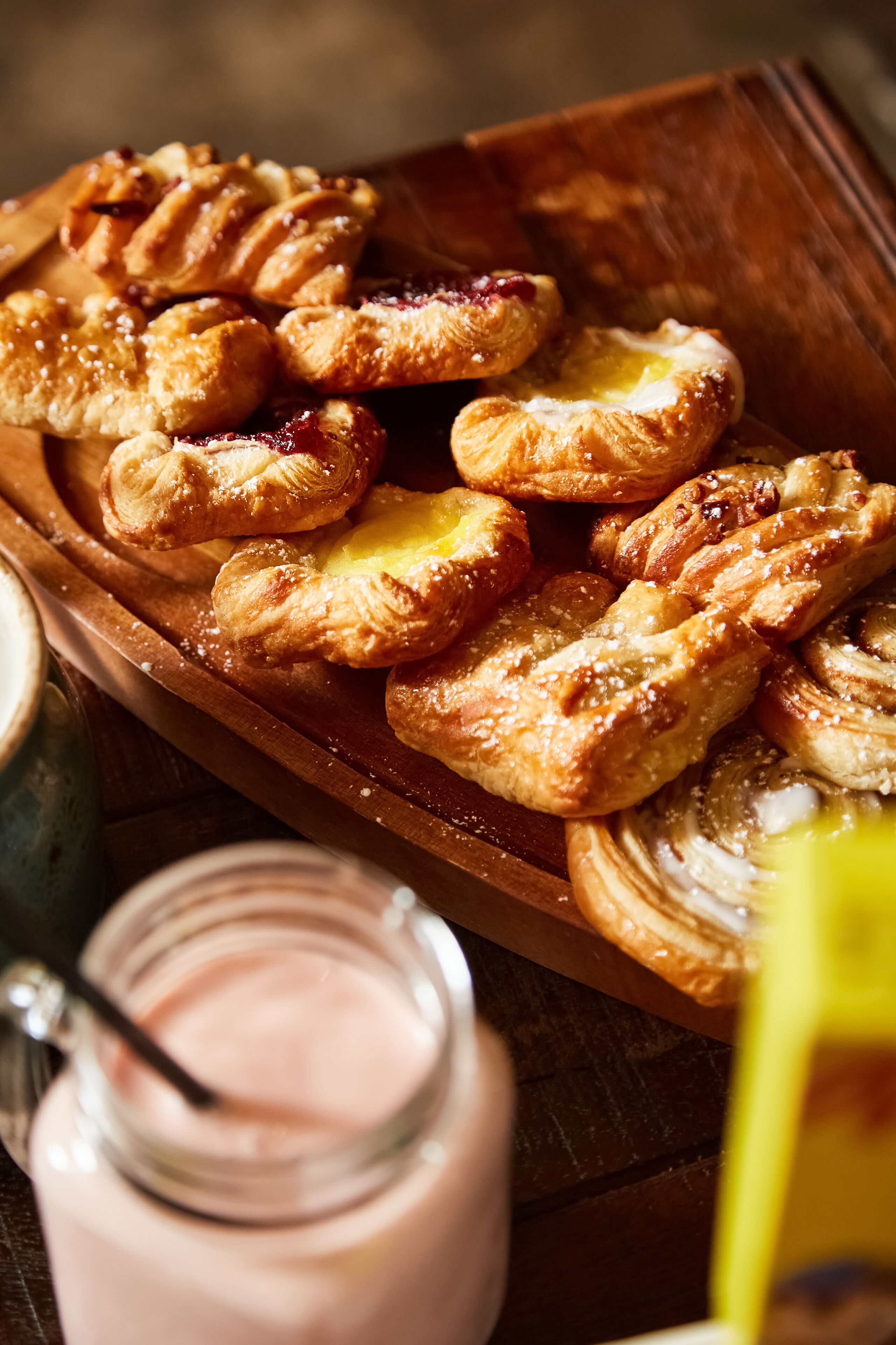 A wooden tray filled with pastries and a jar of pink dessert.
