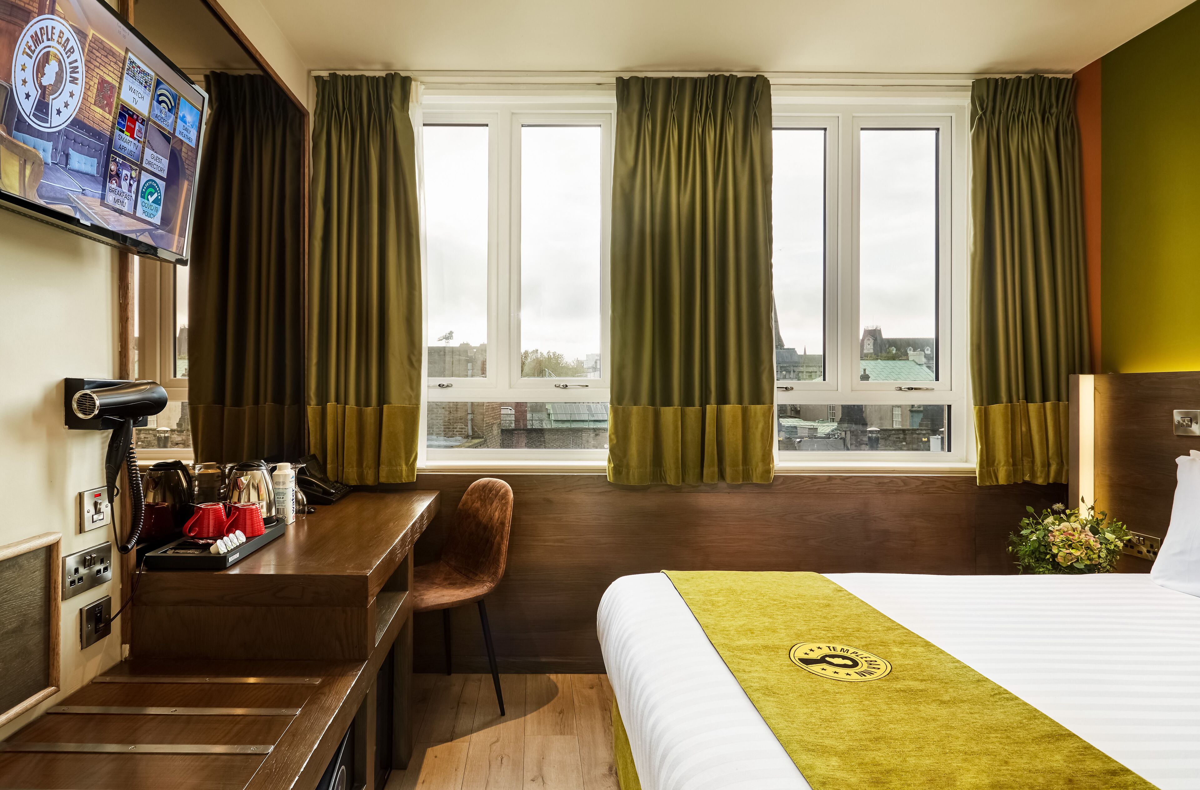 A hotel room with a bed, a desk, a chair, a TV, and a window with curtains.