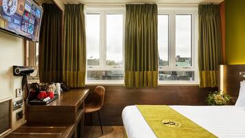A hotel room with a bed, a desk, a chair, a TV, and a window with curtains.