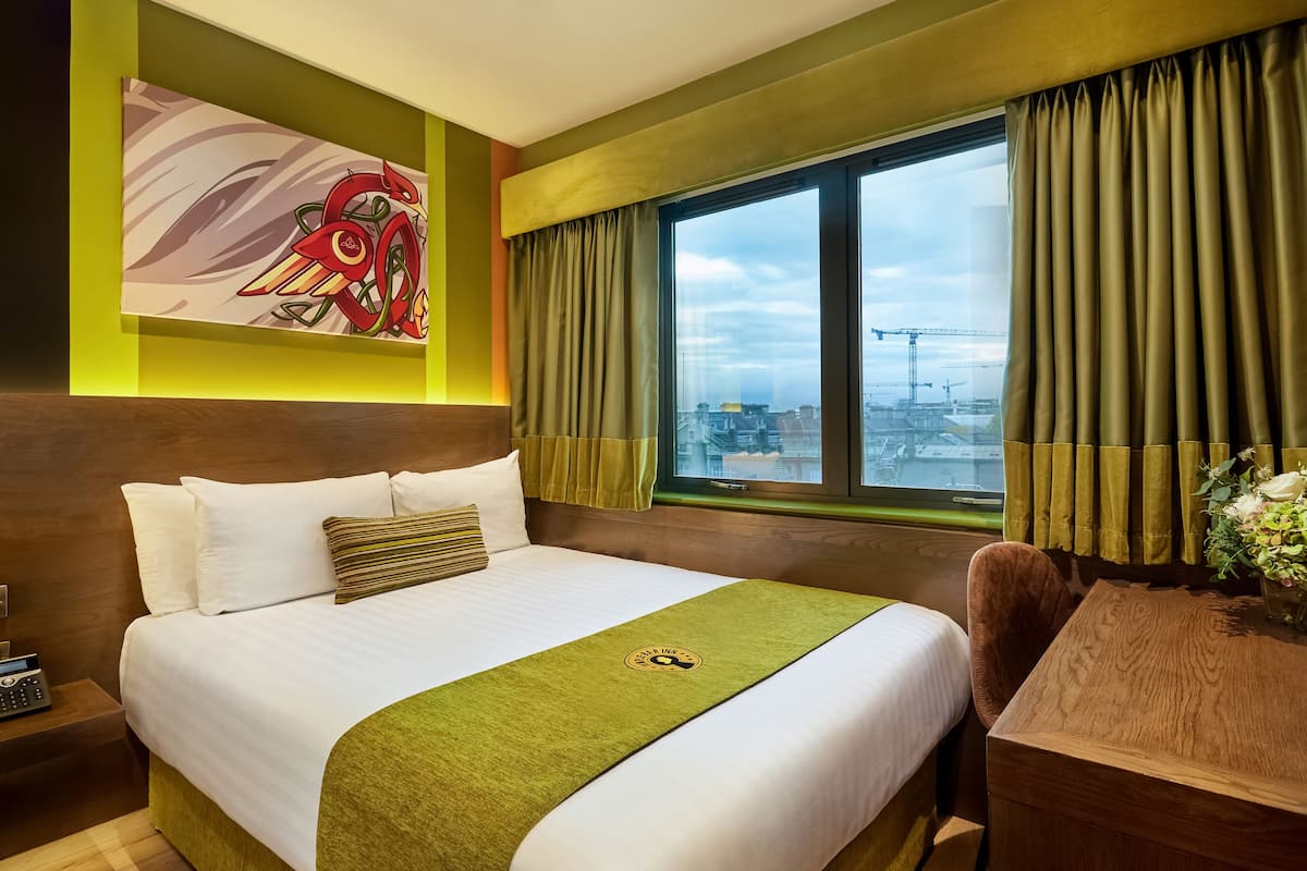 A hotel room with a large bed, a desk, and a window with curtains.
