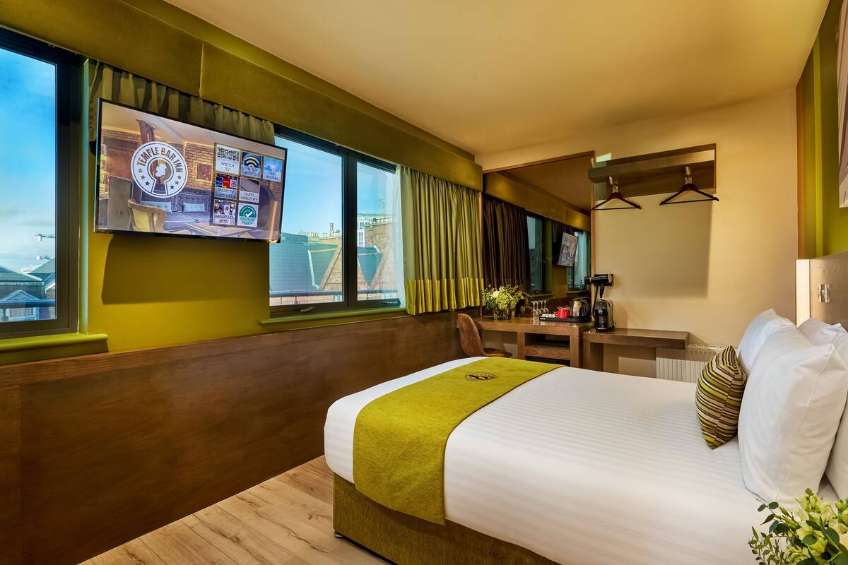 A hotel room with a large bed, a desk, a chair, a television mounted on the wall, and a view of the cityscape.