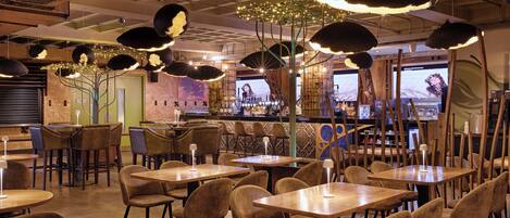 A restaurant interior with multiple tables and chairs, pendant lighting, and a bar area.