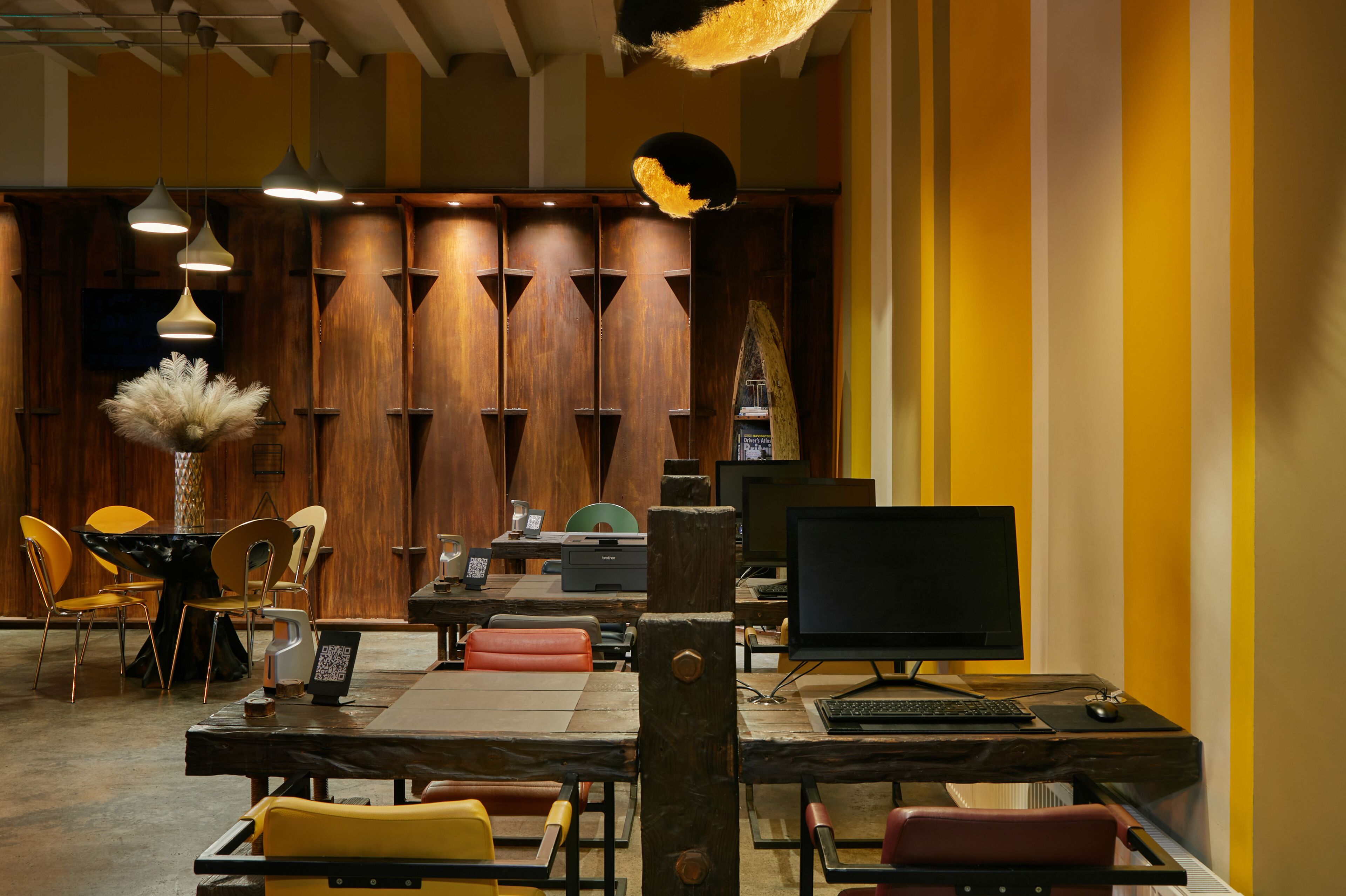 Un intérieur moderne avec des lambris en bois, un coin repas avec des chaises jaunes et un bureau informatique doté d’un écran et d’un clavier.