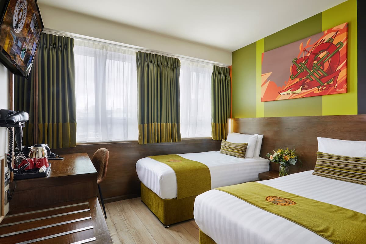 A hotel room with two beds, a desk with a telephone, and a painting on the wall.