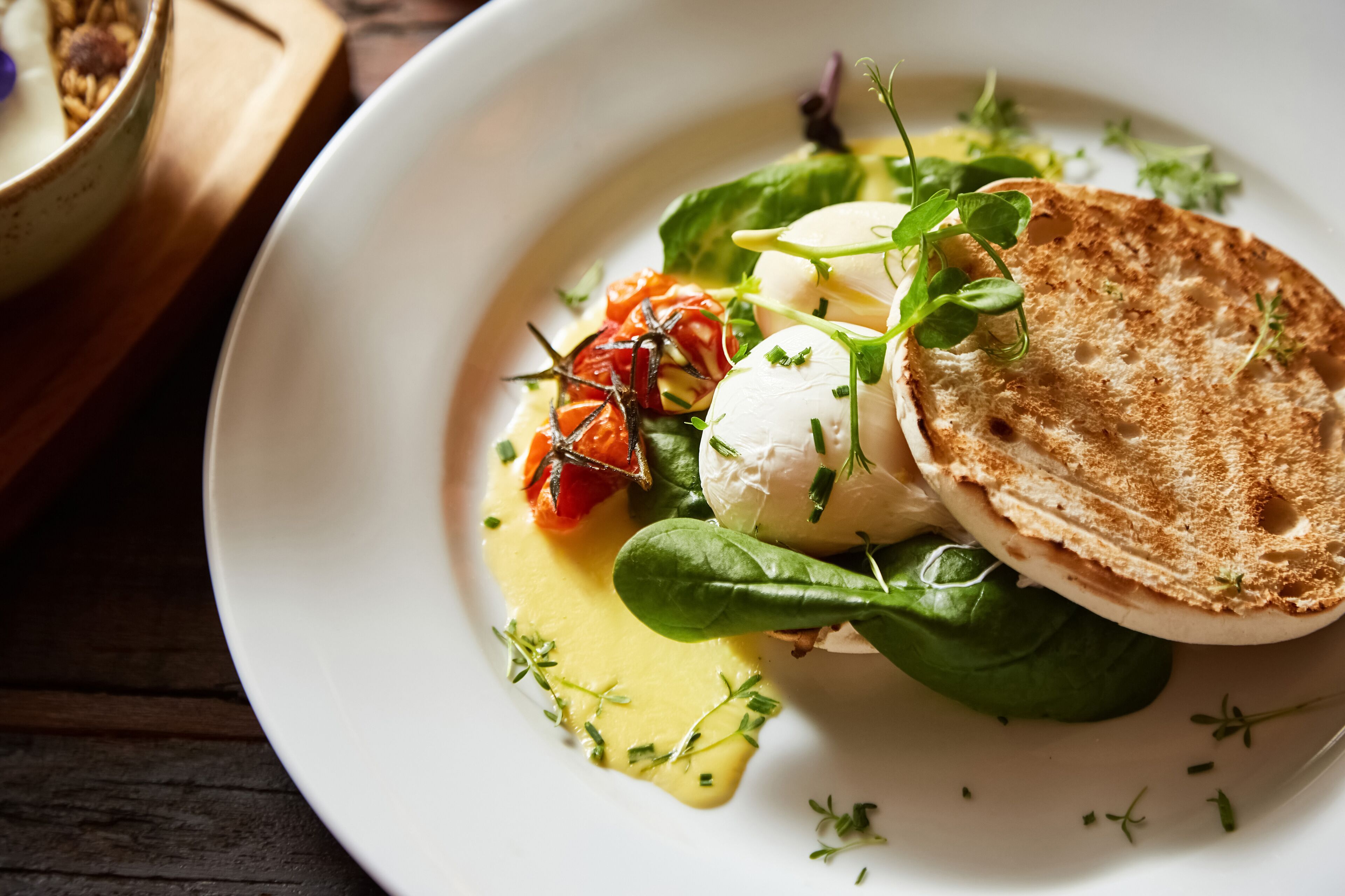 A plate with a poached egg, spinach, cherry tomatoes, and a slice of toasted bread on a white plate.