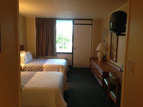 A hotel room with two beds, a dresser, a mirror, and a window with curtains.