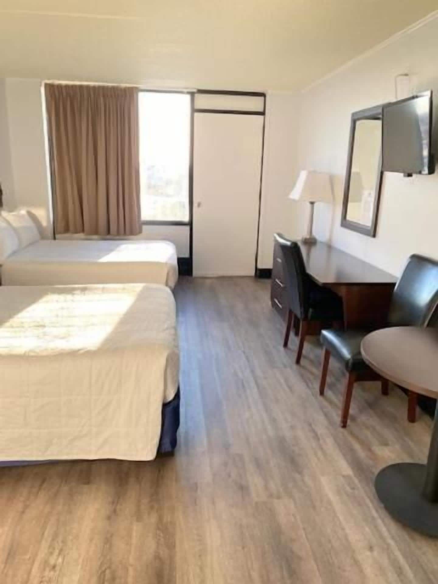 A hotel room with two beds, a desk, a chair, a lamp, and a mirror.