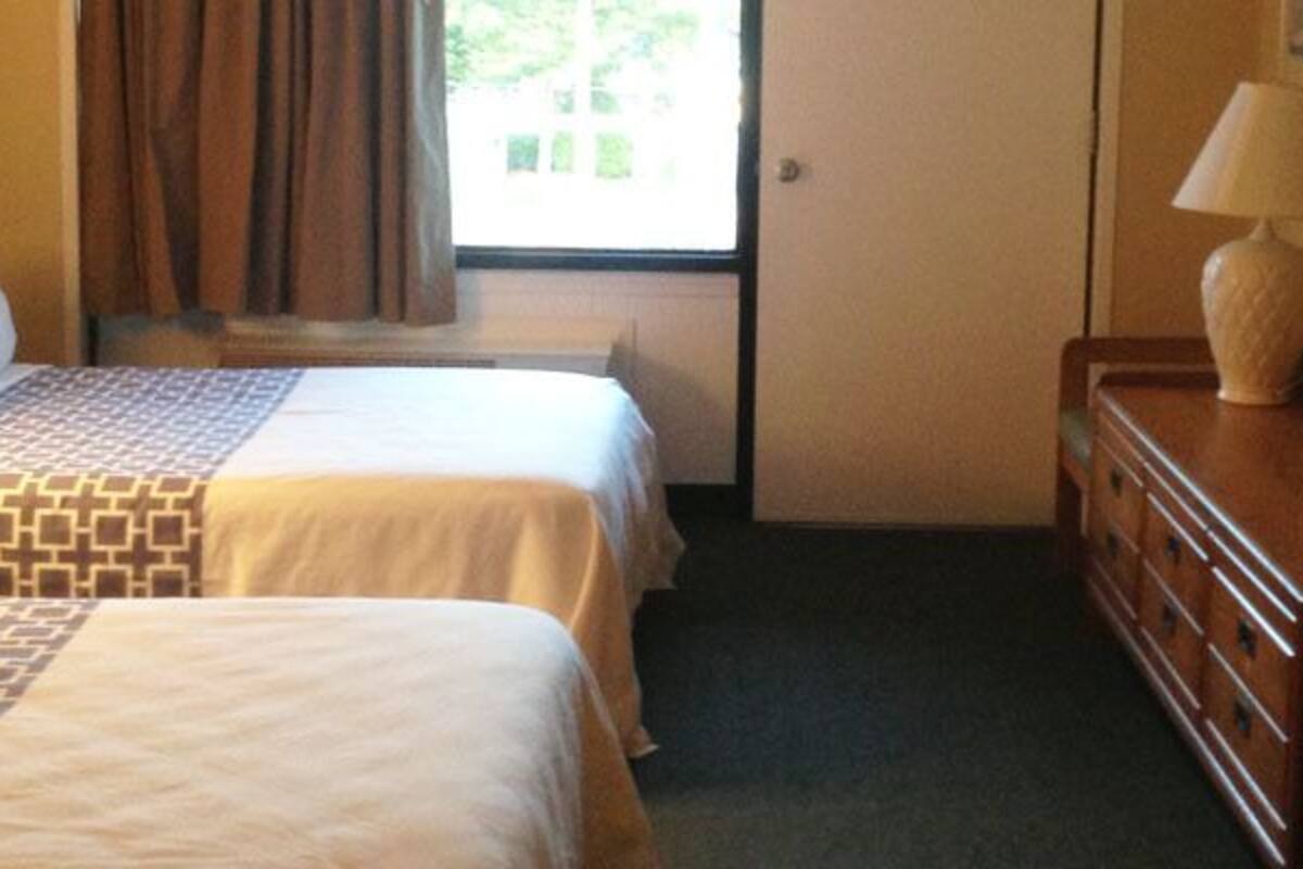 A hotel room with two beds, a dresser, a mirror, and a window with curtains.