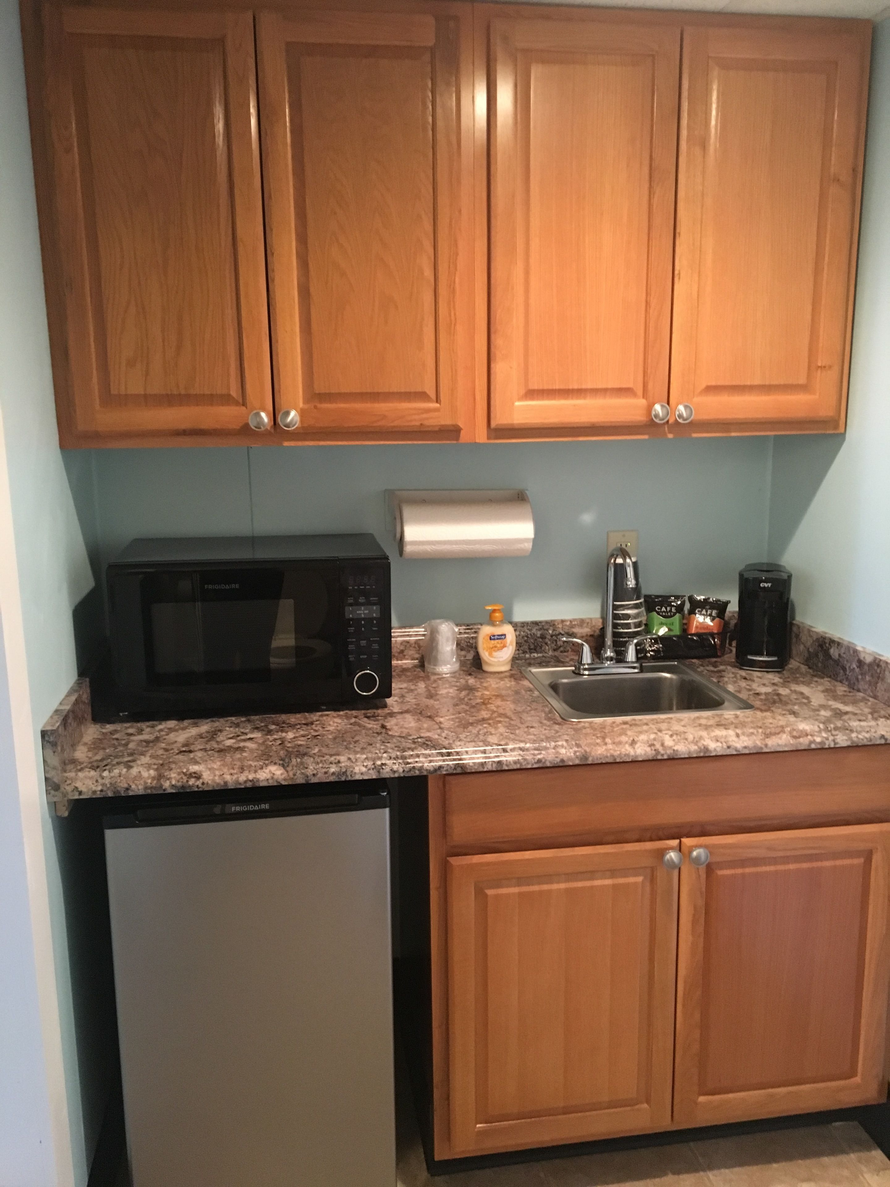 Cocina con armarios de madera, microondas, cafetera y lavamanos.