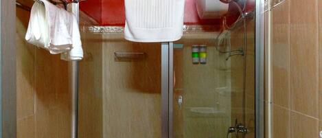 A glass-enclosed shower with a handheld showerhead, a towel rack with towels, and a control panel with a green indicator light.