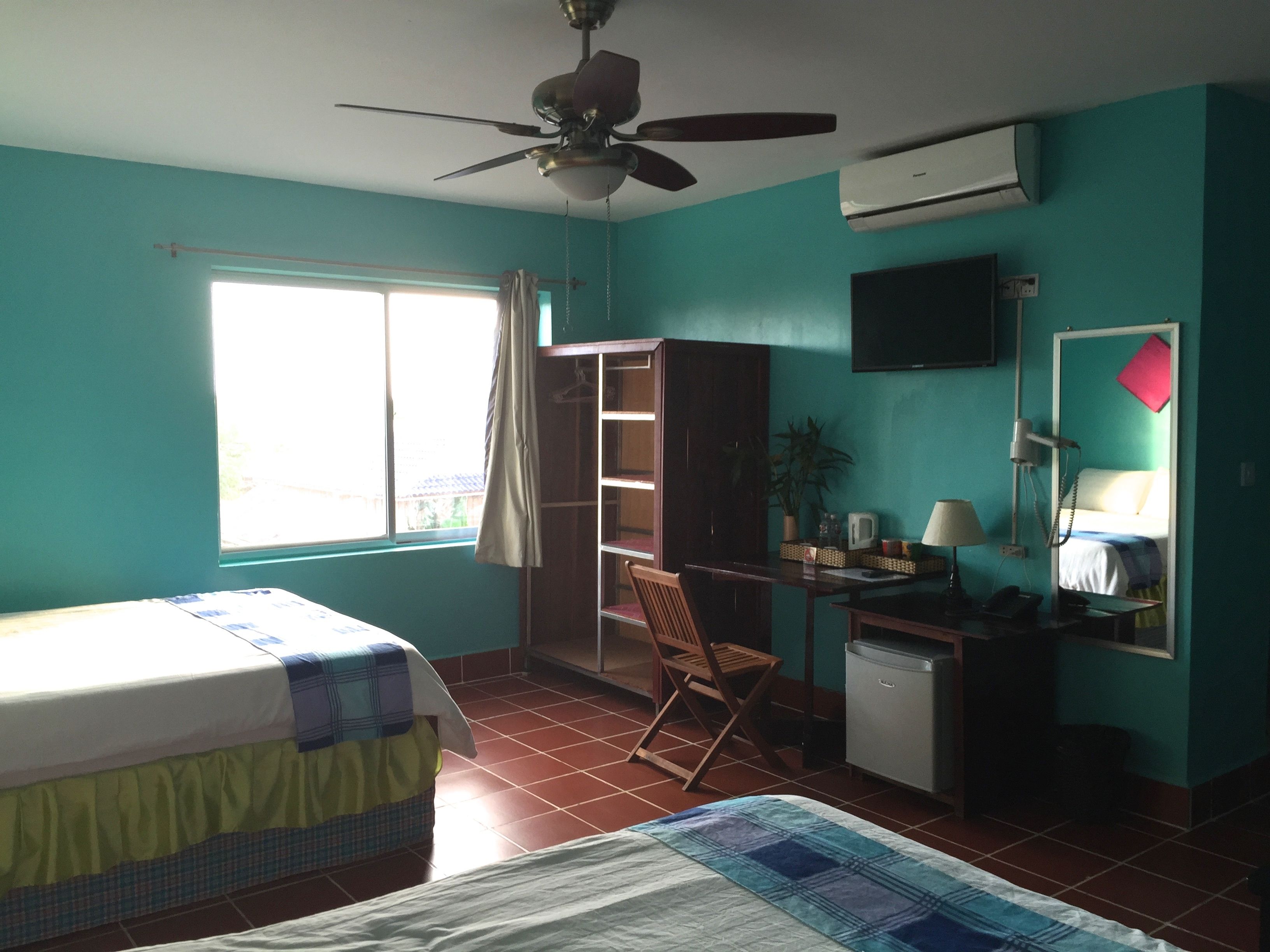 Una habitación con cama, escritorio con silla, armario, televisor y aire acondicionado.