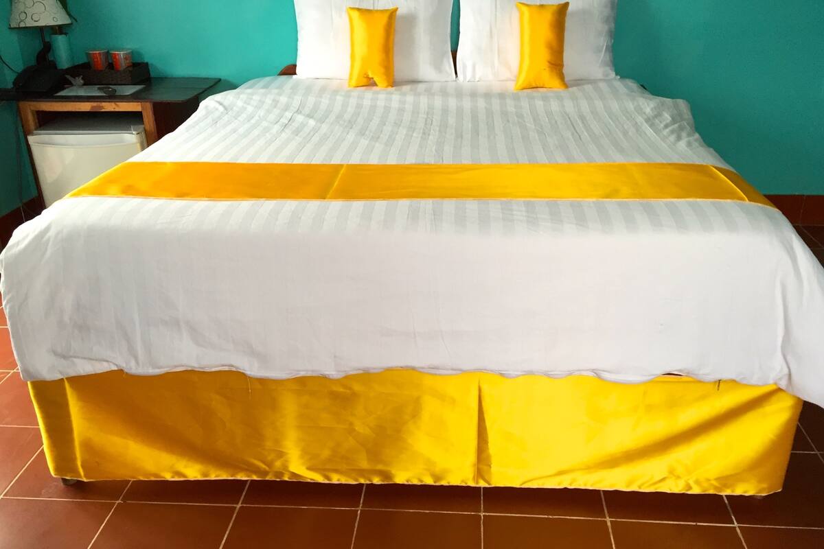 A bed with a white and yellow bedspread, two white pillows, and a yellow accent pillow.