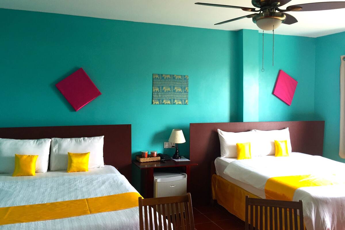A hotel room with two beds, teal walls, and a ceiling fan.