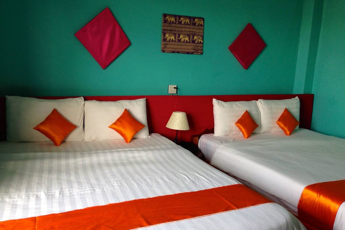 A hotel room with two beds, each with white bedding and orange accents, a red headboard, and teal walls.