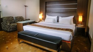 A hotel room with a large bed, a bench, a desk, two chairs, and bedside lamps. - Furaya Hotel (Pekanbaru)