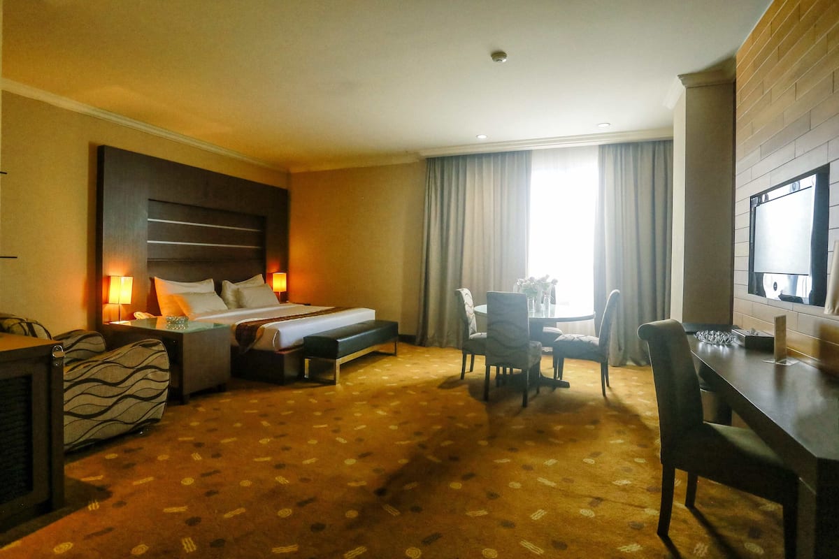 A hotel room with a bed, bedside table, lamp, chair, desk, and a large window with curtains.