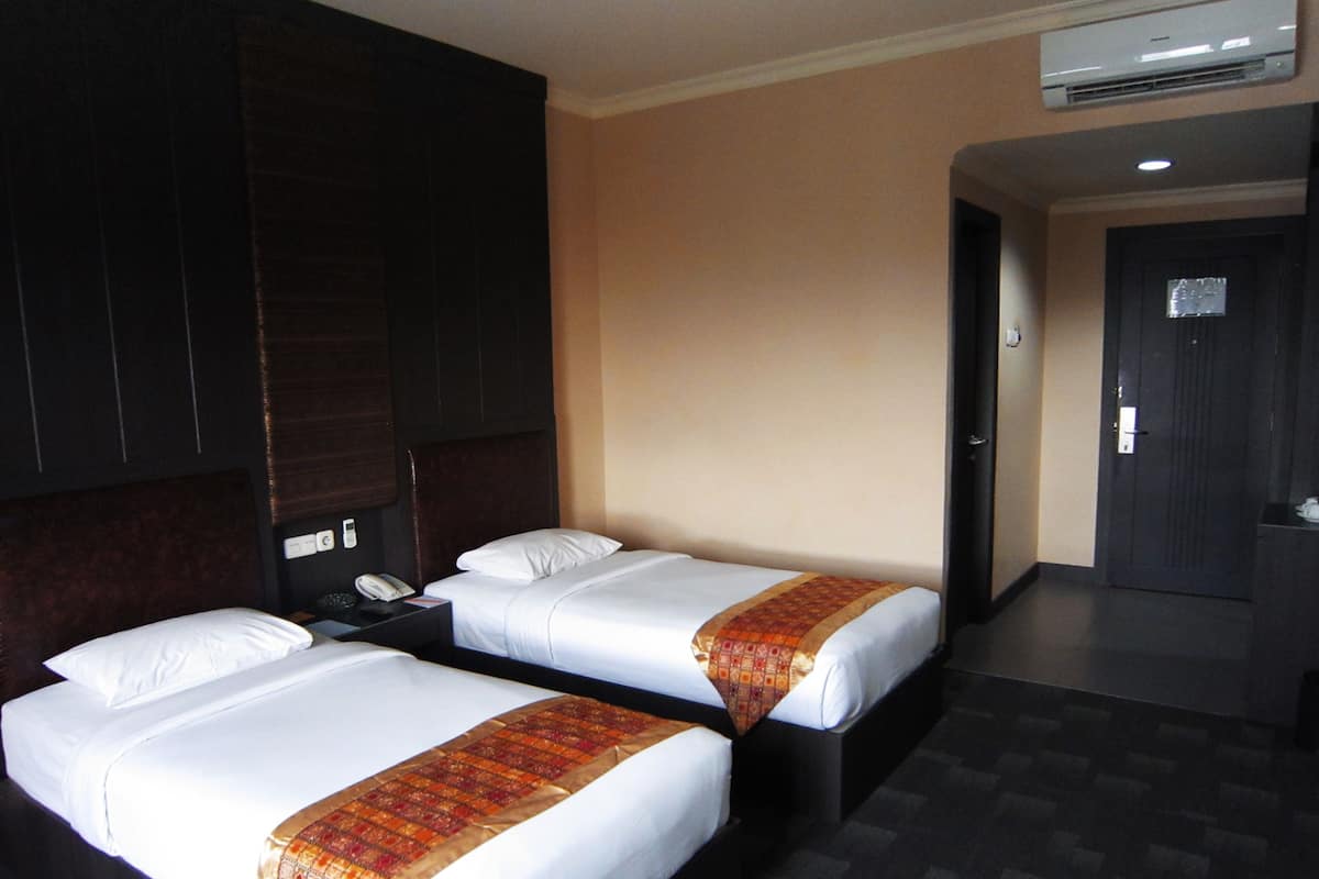A hotel room with two beds, a telephone, and an air conditioning unit.