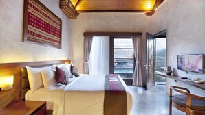 A hotel room with a bed, bedside table, desk, chair, TV, and a view of the ocean. - Bracha Villas (Seminyak)