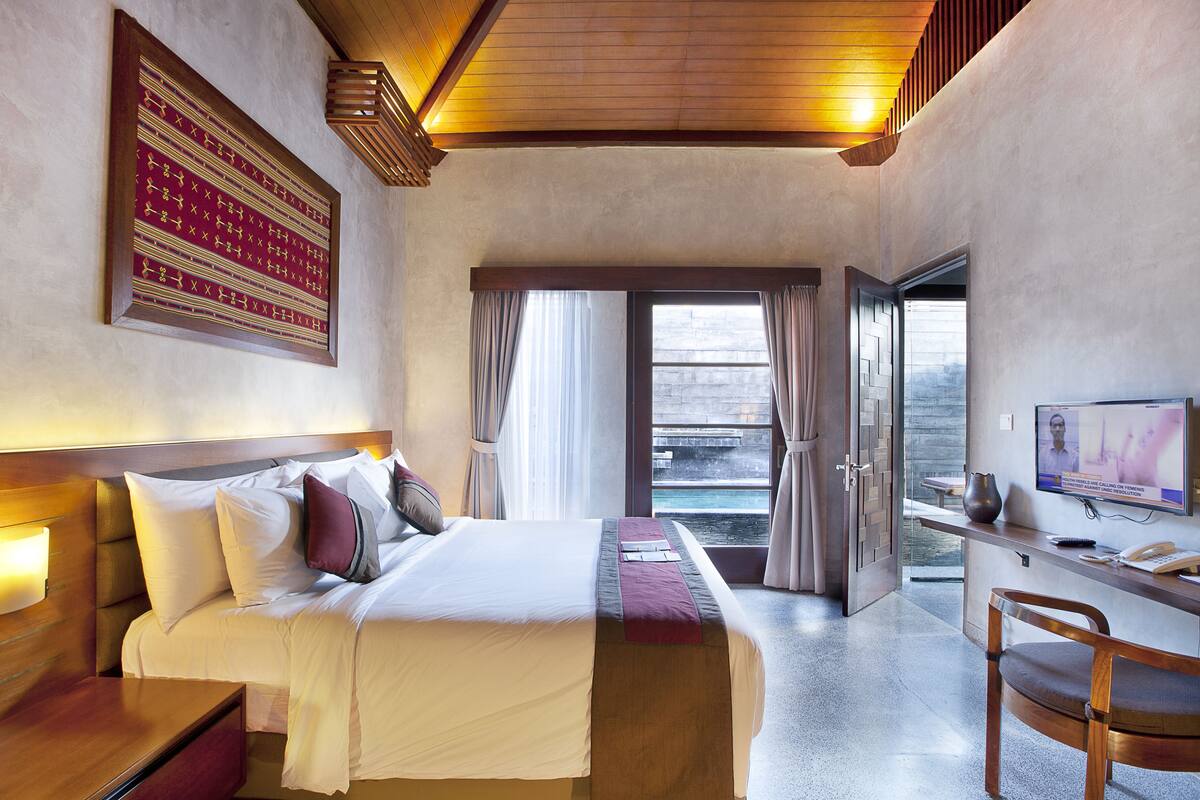Habitación de hotel con cama, mesita de noche, escritorio, silla, televisor y vista al océano.