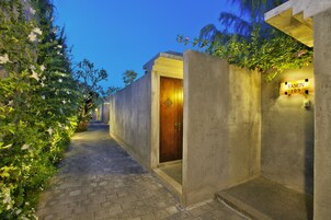 Un sendero estrecho que lleva a la entrada de un edificio, con una puerta de madera, un muro de hormigón y un letrero que dice "RAMIN 109".