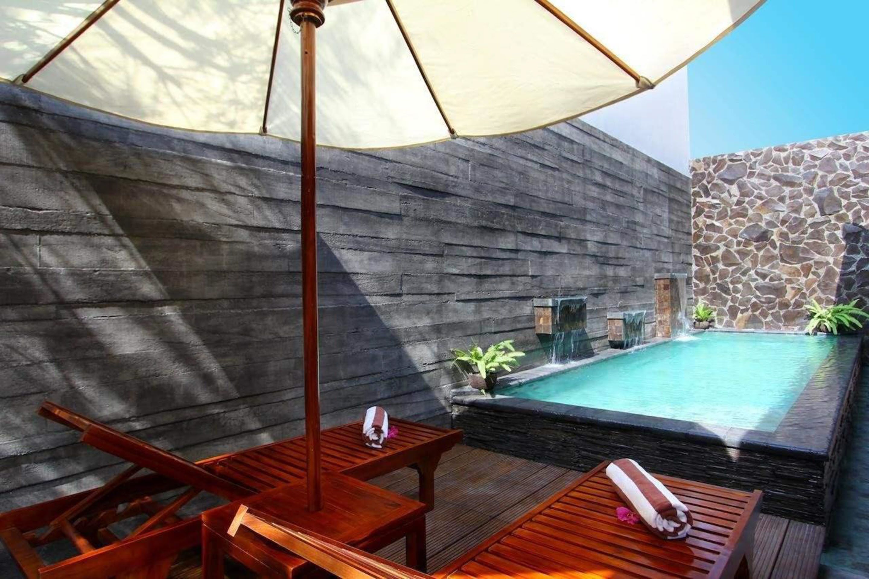 A wooden deck with a pool, stone walls, and a hanging umbrella.
