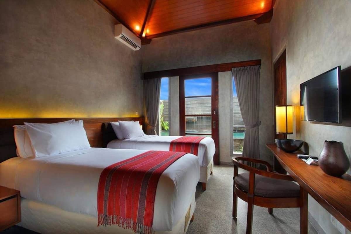 Una habitación de hotel con dos camas, un escritorio con silla, televisión y un ventanal grande.