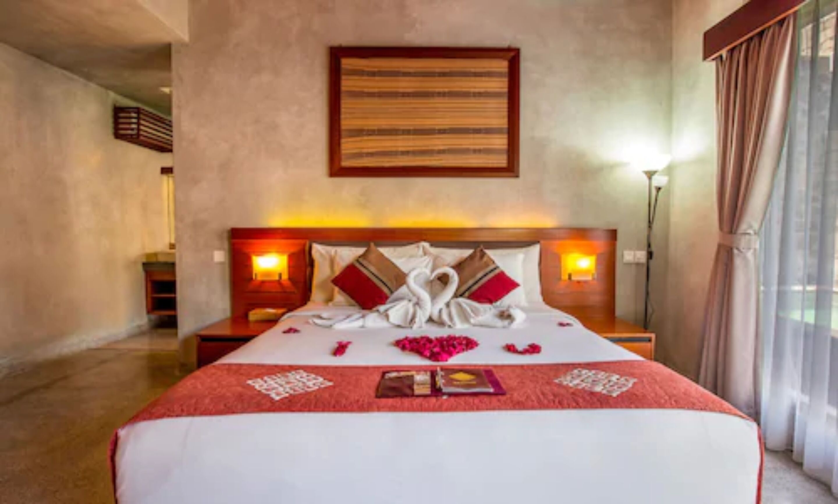 Habitación de hotel con una cama grande, dos lámparas de noche, un cuadro enmarcado en la pared y una ventana con cortinas.