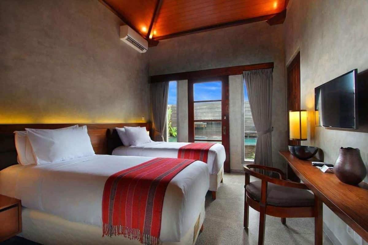 Habitación de hotel con dos camas, un escritorio, una silla, un televisor y un amplio ventanal con vistas.