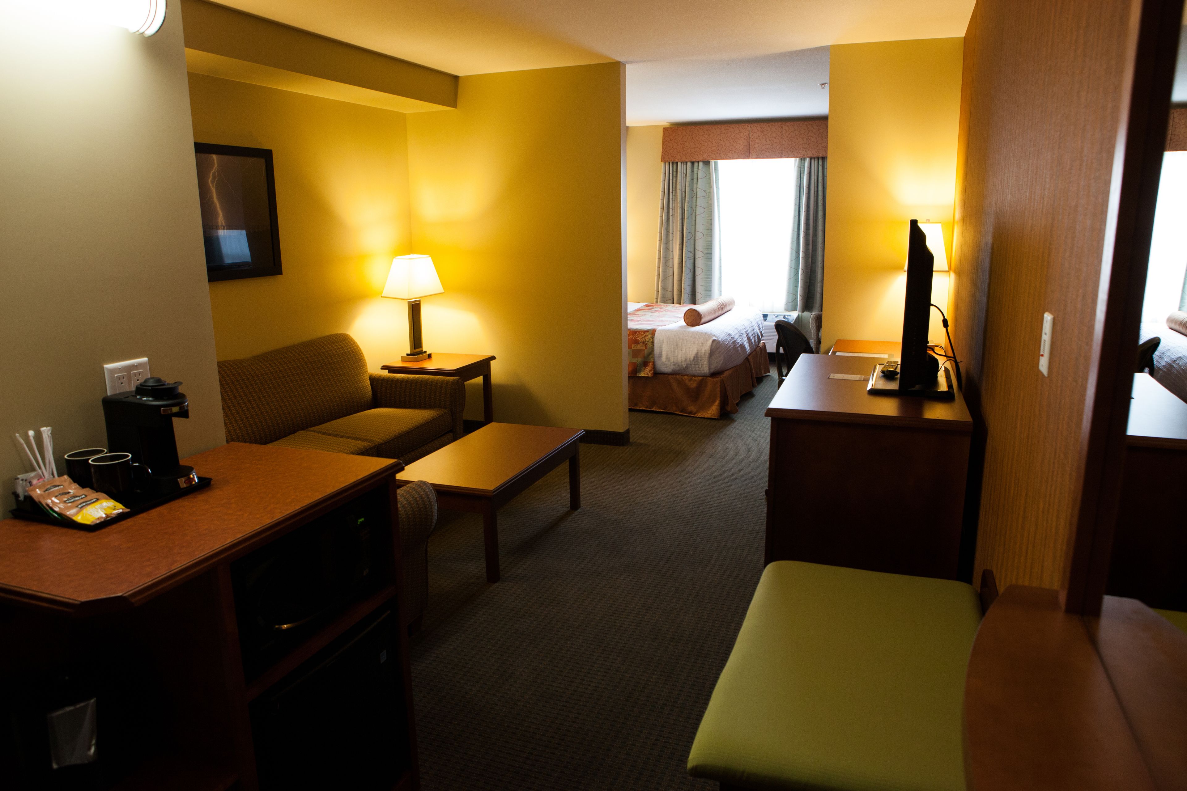 A hotel room with a bed, a desk, a chair, a sofa, a lamp, and a television.